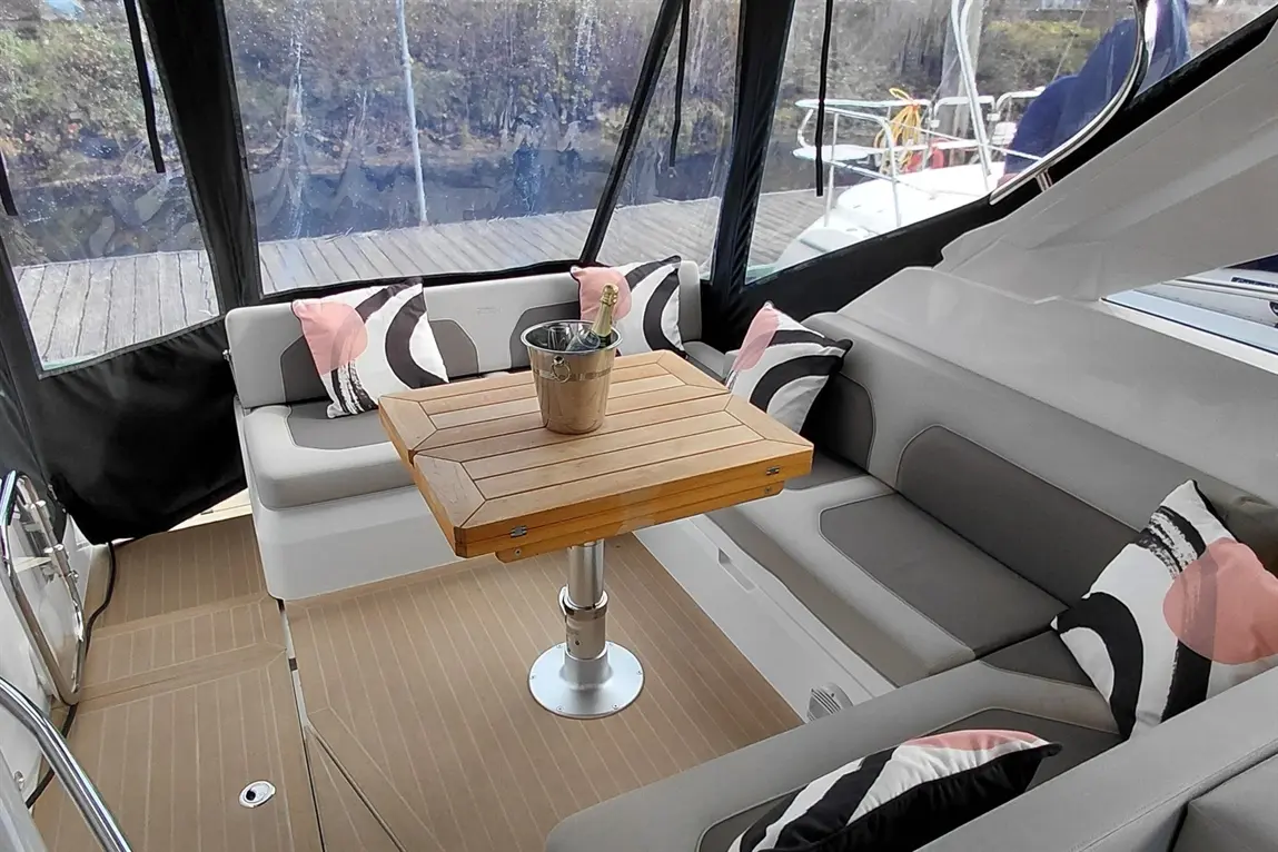 Modern boat interior featuring grey seating, decorative cushions, a wooden table, and a champagne bucket on display.